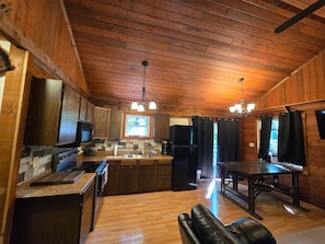 A wooden cabin interior with a kitchen, dining area, and a fireplace.
