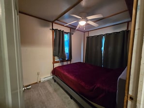 Ein Schlafzimmer mit einem Einzelbett, einem Deckenventilator und einem Fenster mit Vorhängen.