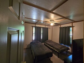 A room with two single beds, a ceiling fan, and a television.