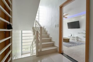 A modern interior with a staircase leading to a living area, a flat-screen TV, and a view through a glass door. - Luxe Stay in Zona Colonial (Santo Domingo Este)