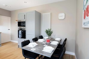 A modern dining area with a grey table set for six, black chairs, a potted plant, and a wall clock.