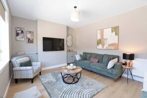 A modern living room with a sofa, armchair, coffee table, and artwork on the walls.