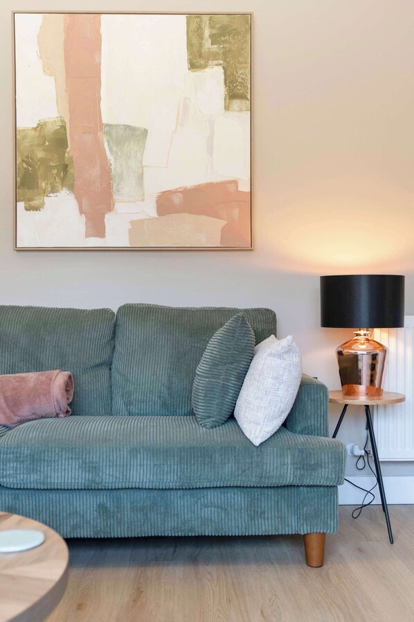 A living room with a green sofa, a round side table, a lamp, and a large abstract painting on the wall.