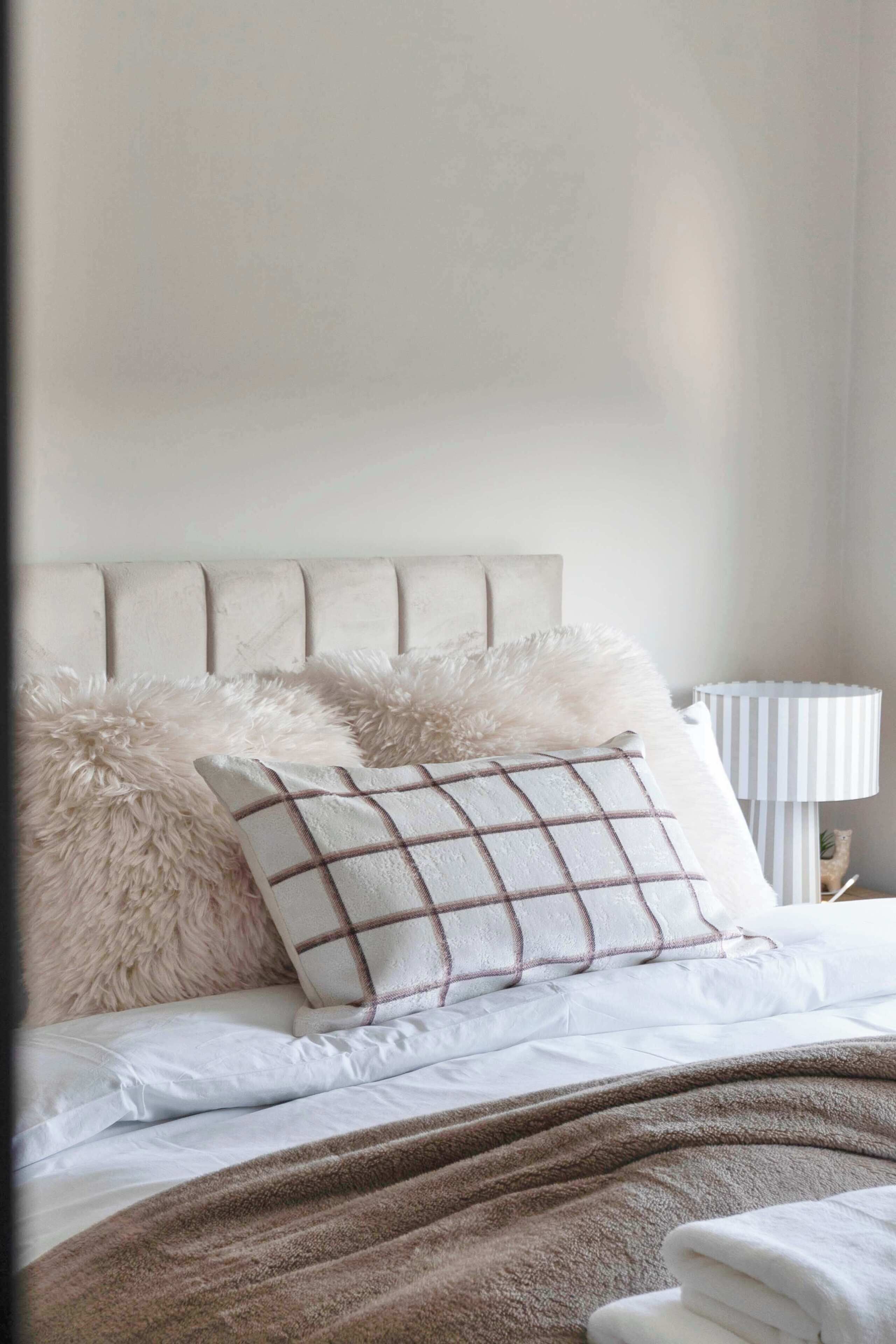 Ein Bett mit weißer Bettwäsche, flauschigen Kissen und einem Kissen in Karomuster.