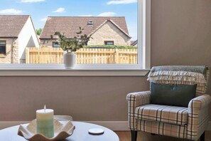 A room with a view of houses through a window, a chair with a plaid blanket, and a candle on a tray. - Forthside House - 3 Bedroom House, Kincardine (Kincardine)