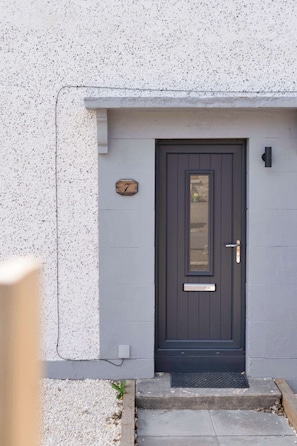 A dark-colored door with a small window, a number plaque, and a mailbox on a textured wall. - Forthside House - 3 Bedroom House, Kincardine (Kincardine)