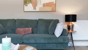 Ein grünes Sofa mit Kissen, ein Tisch mit Kerze und eine Stehlampe.