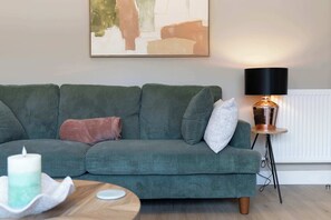 A green sofa with a cushion, a table with a candle, and a floor lamp. - Forthside House - 3 Bedroom House, Kincardine (Kincardine)