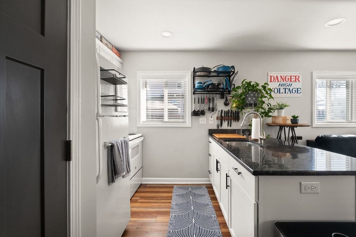 A modern kitchen with a black countertop, white cabinets, and a black and white patterned rug.