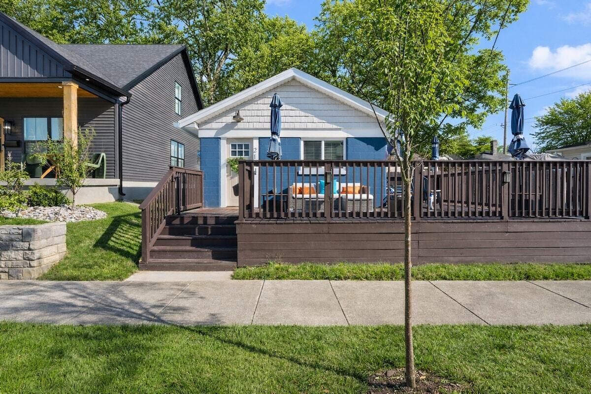 A two-story house with a covered deck, a stone retaining wall, and a well-maintained lawn.