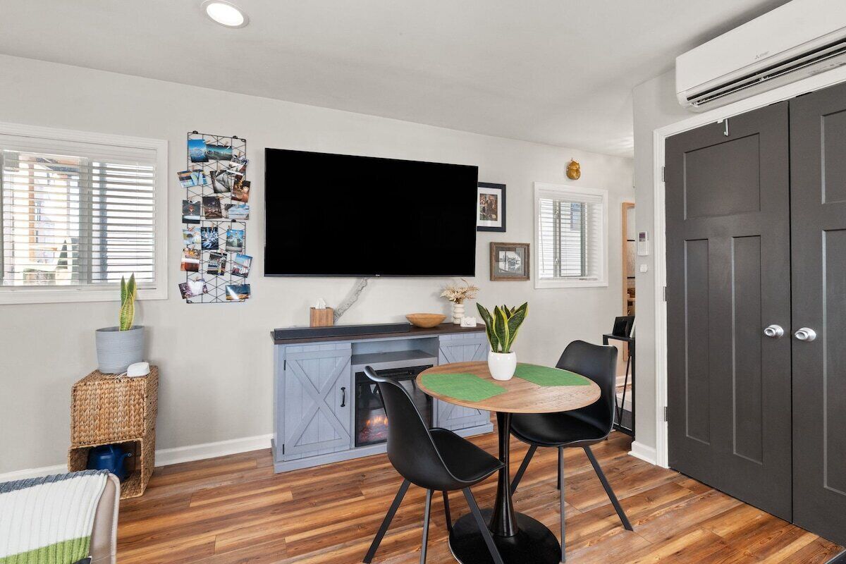 Een moderne woonkamer met een flatscreen televisie, een eethoek met een ronde tafel en stoelen, een open haard en een grote donkere deur.