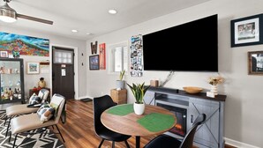 Ein modernes Wohnzimmer mit Kamin, Flachbildfernseher und Essbereich mit rundem Tisch und Stühlen.