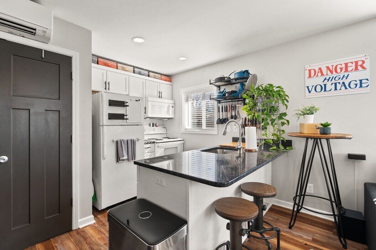 A modern kitchen with white cabinetry, a black countertop island, and a 'DANGER HIGH VOLTAGE' sign.