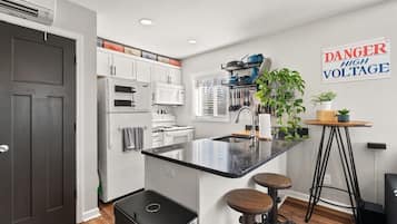 A modern kitchen with white cabinetry, a black countertop island, and a 'DANGER HIGH VOLTAGE' sign.