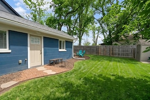 A residential backyard with a blue house, a wooden fence, and a lawn.