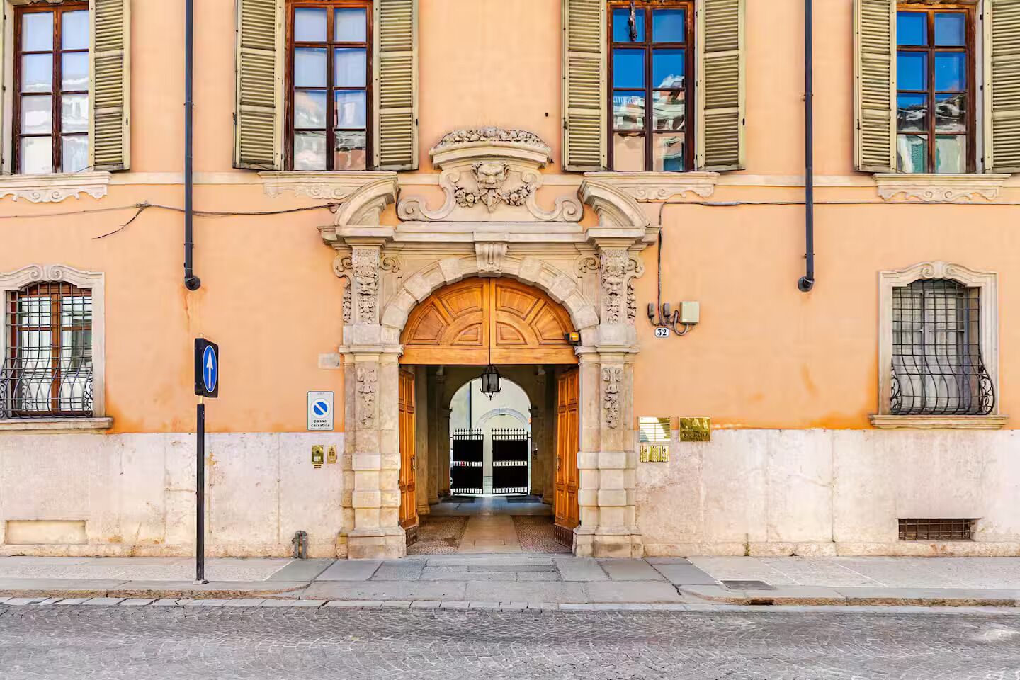 A building facade with a central entrance, ornate stone archway, and multiple windows with shutters.
