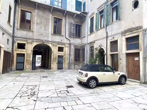 Ein Innenhof mit einem geparkten Auto in der Mitte, umgeben von Gebäuden mit rundbogigen Eingängen und vergitterten Fenstern.