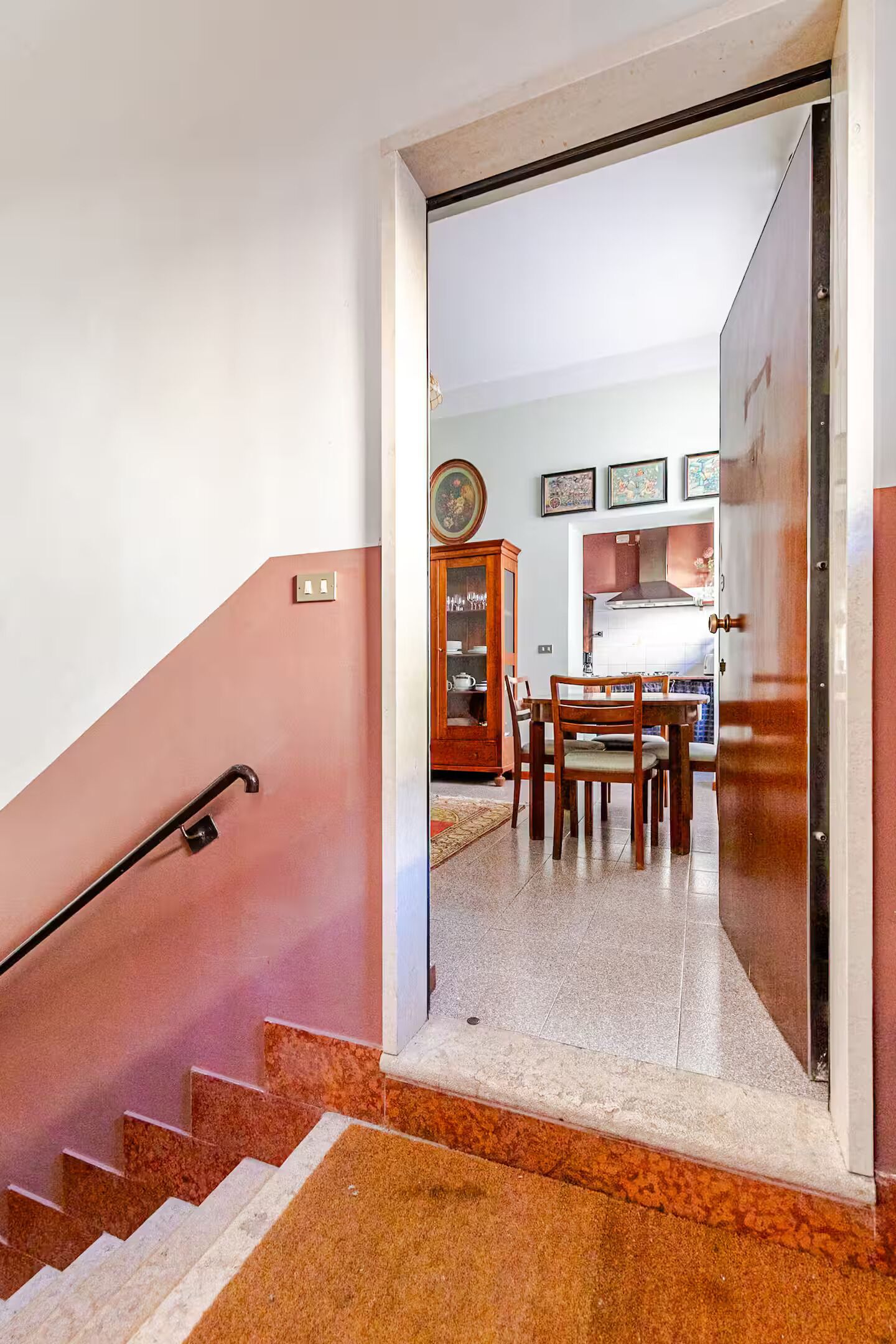 A staircase leading to a dining area with a table and chairs, a cabinet with glass doors, and a wall with framed pictures.