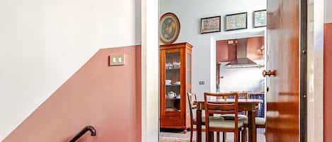 Un escalier menant à un espace repas comprenant une table et des chaises, un meuble avec des portes en verre et un mur orné de tableaux encadrés.