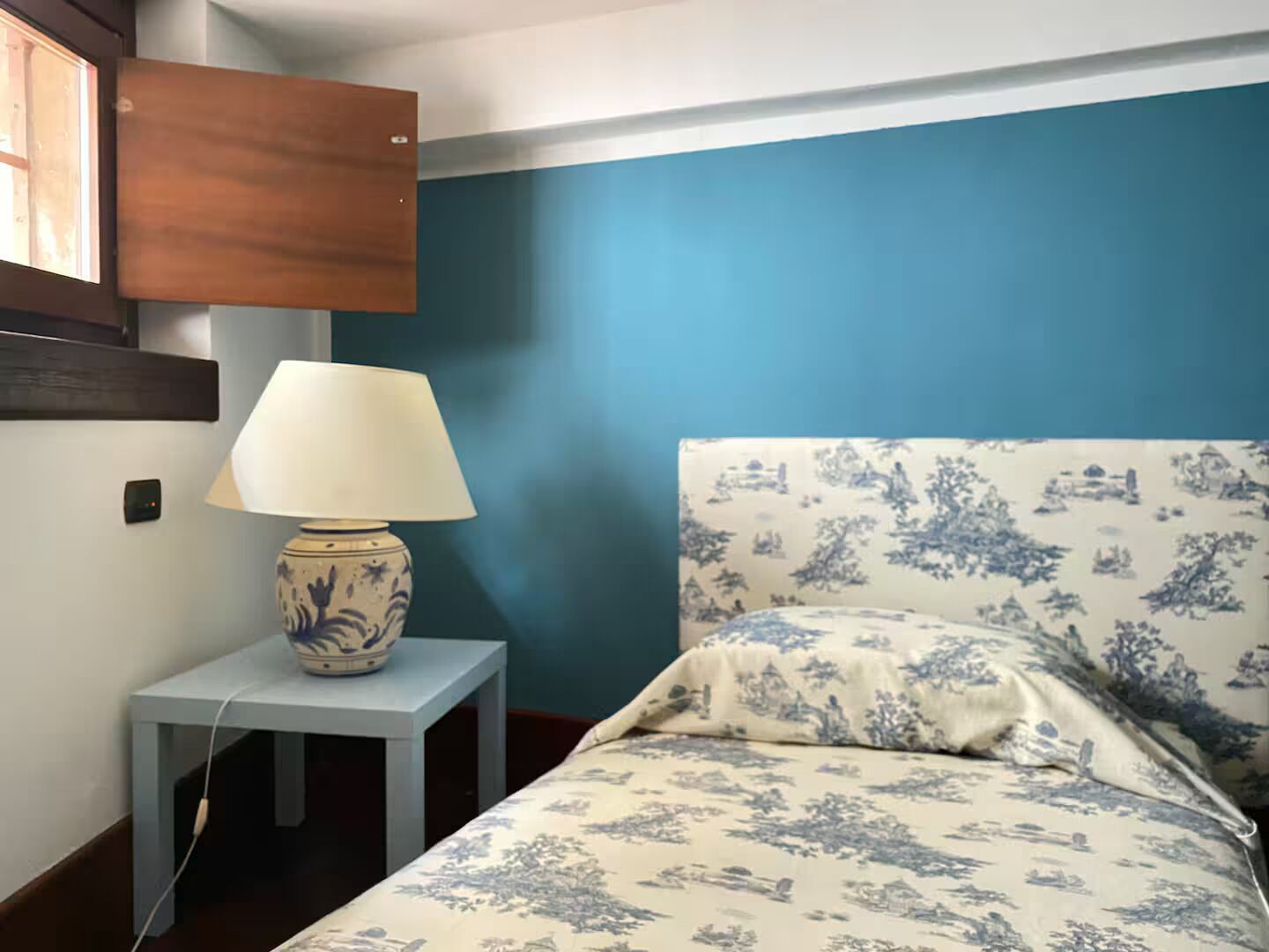 Quarto com cama, mesa de cabeceira com abajur e armário fixado na parede.