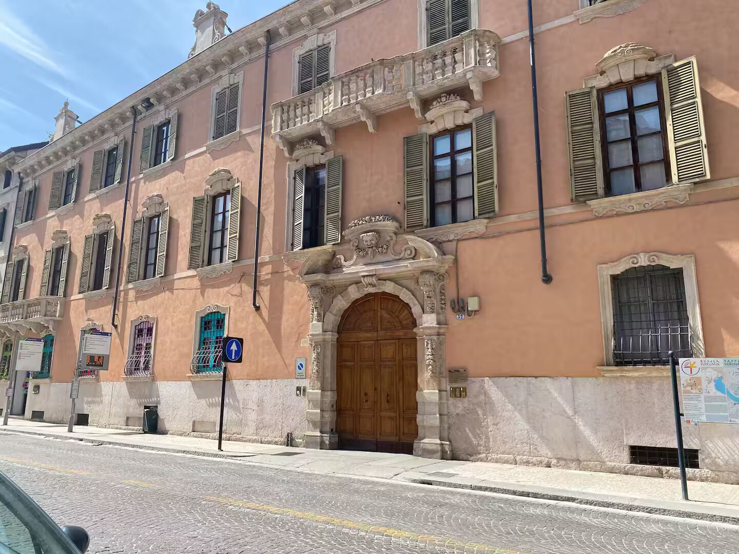 A historic building with a central wooden door, multiple windows with shutters, and a decorative balcony.