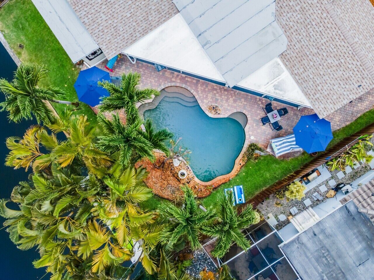 An aerial view of a property with a swimming pool, patio furniture, and lush greenery.