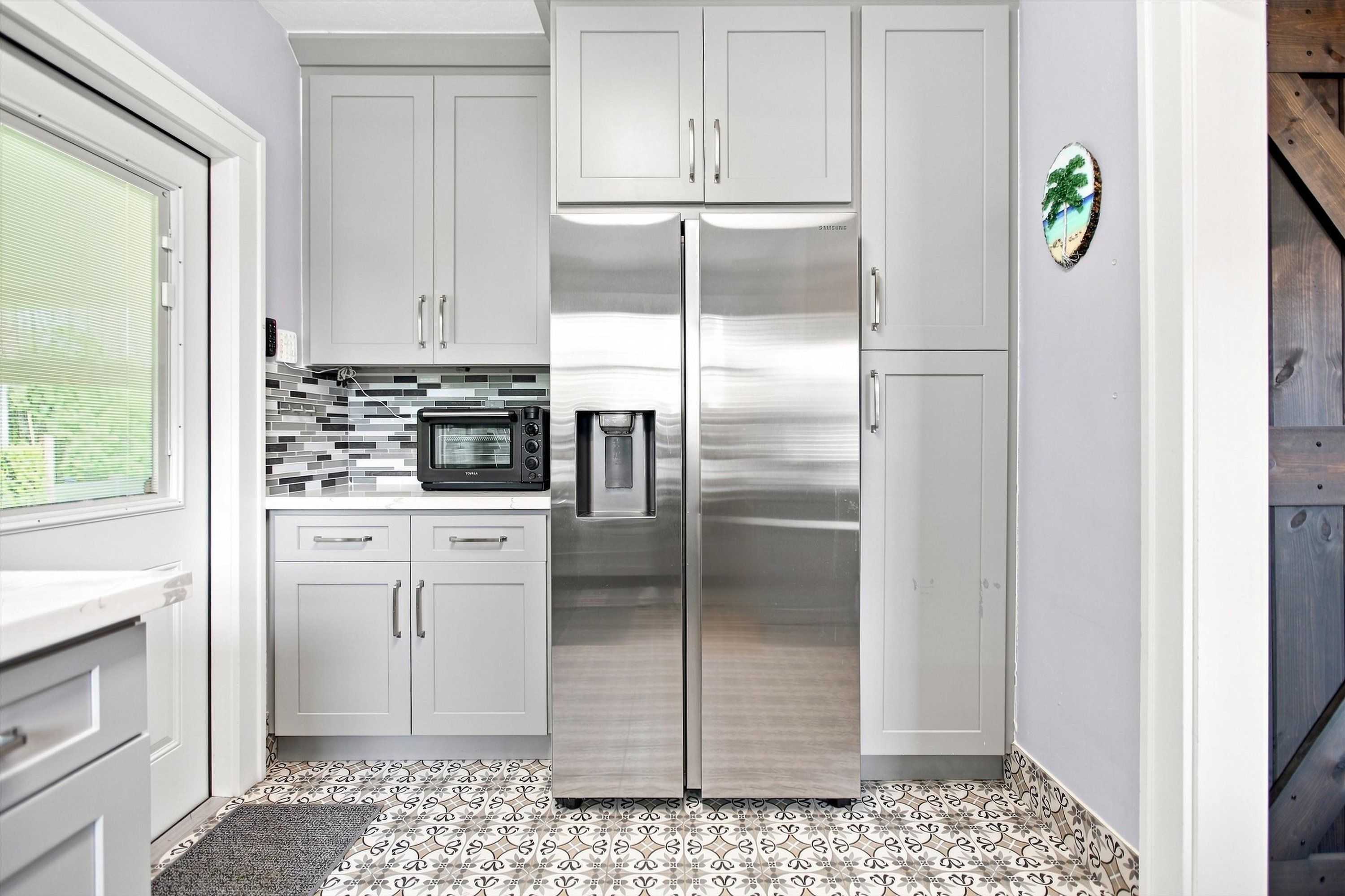 A kitchen with white cabinets, a stainless steel refrigerator, a microwave, and a toaster.