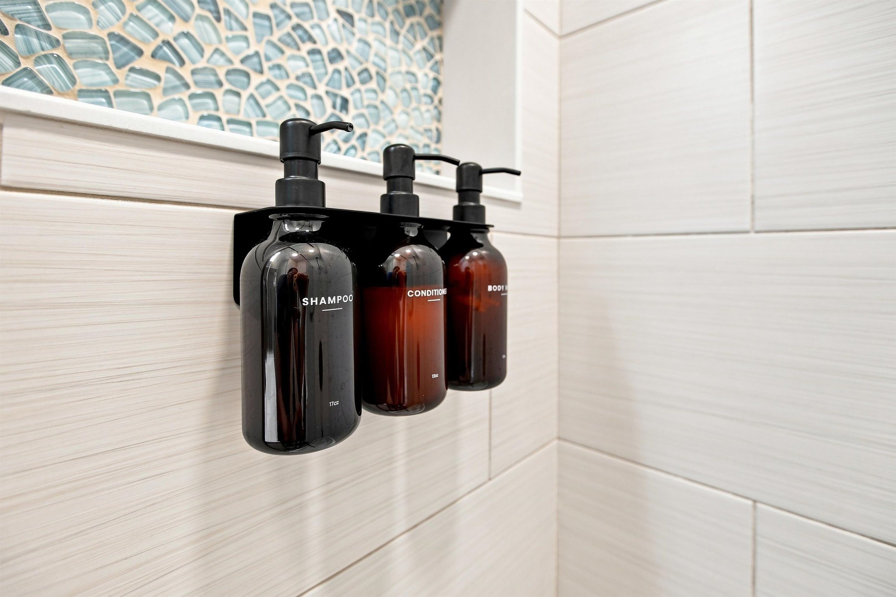 A bathroom with a wall-mounted soap dispenser and a shower head.
