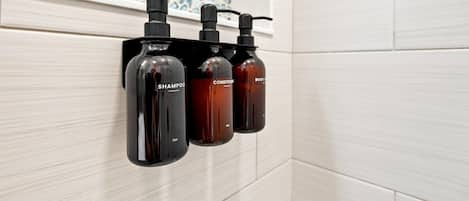 A bathroom with a wall-mounted soap dispenser and a shower head.
