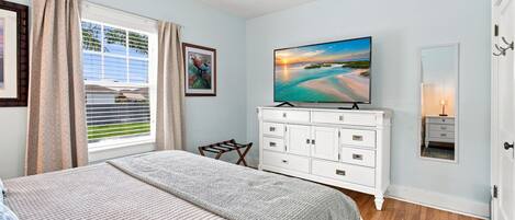 A bedroom with a bed, a dresser, a television, and a window with curtains.