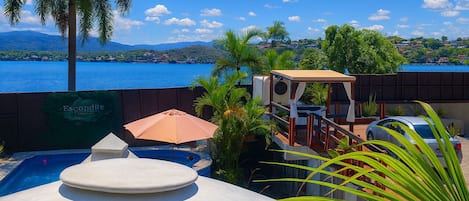 A pool area with a view of a body of water and hills, a covered seating area, and a sign for 'Escondite'.