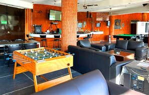 A room with a foosball table, sofas, a dartboard, and a bar area with a television. - Escondite Teques / Alberca climatizada, diversión y espacio para grupos (Tequesquitengo)