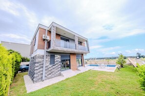Ein modernes, zweistöckiges Haus mit Naturstein-Fassade, einem Balkon und einem Swimmingpool im Garten.