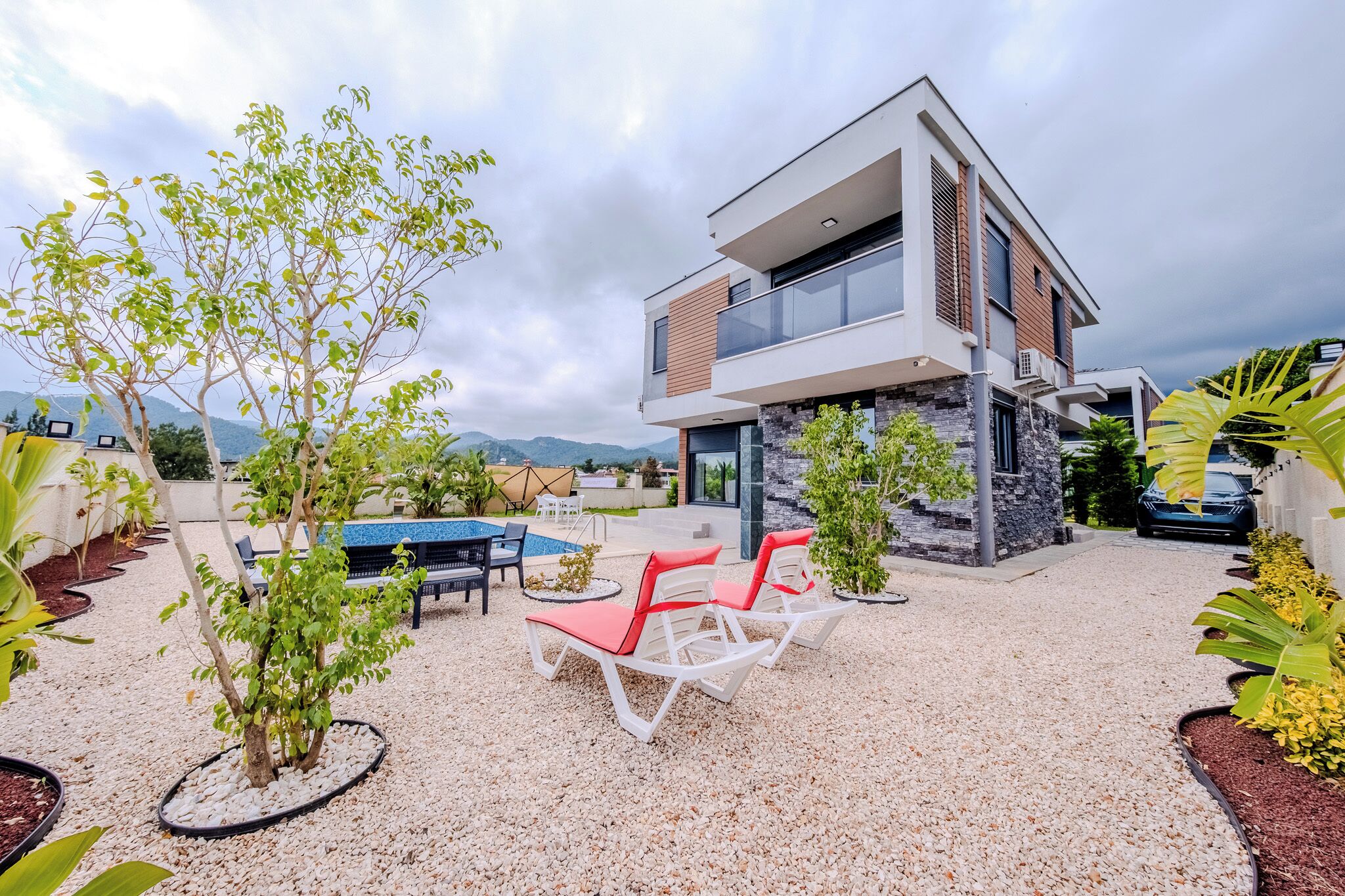 Un edificio moderno de dos pisos con terraza en la azotea, asientos al aire libre y una piscina.
