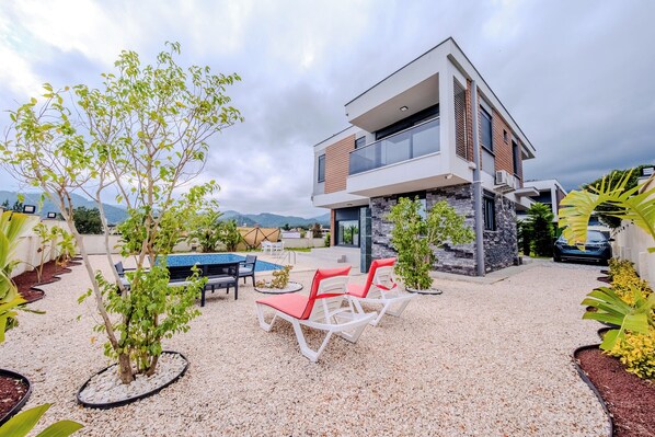 Un bâtiment moderne à deux étages doté d’une terrasse sur le toit, d’un espace extérieur aménagé et d’une piscine.