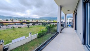A balcony with a view of a green field, buildings, and mountains in the distance.