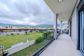 A balcony with a view of a green field, buildings, and mountains in the distance.