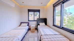A room with two single beds, a small bedside table, a window, and an air conditioning unit.