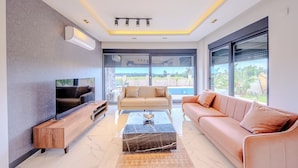 A modern living room with a flat-screen TV, a wooden coffee table, a beige sofa, and a pink sofa.