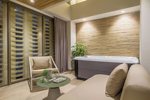 A modern room with a sofa, a massage table, a glass partition, and a potted plant.