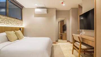 A hotel room with a bed, a desk, a chair, a television, and an air conditioning unit.