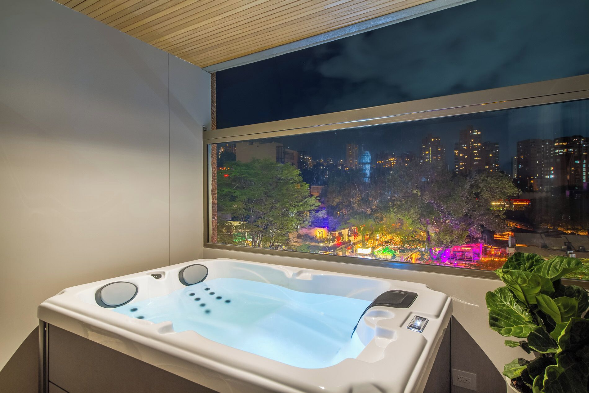 A modern room with a hot tub, a large window overlooking a cityscape at night.