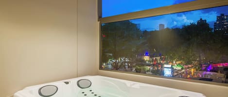 A modern bathroom with a bathtub, a window with a city view, and a wooden ceiling.