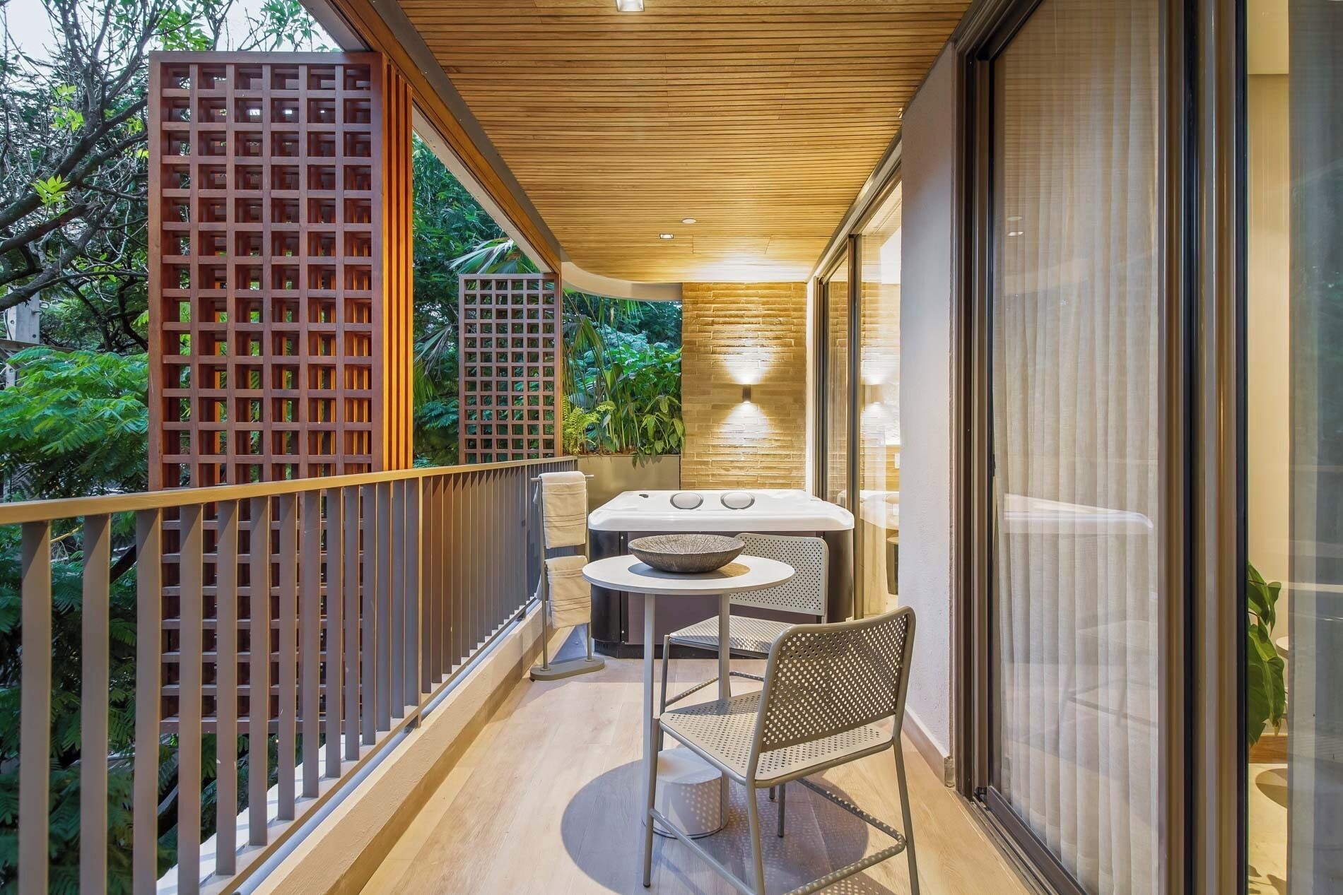A balcony with a wooden railing, a table with a bowl, a chair, and a potted plant.