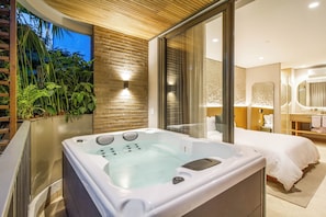 A modern bedroom with a large bathtub, a bed, and a bathroom with a mirror.