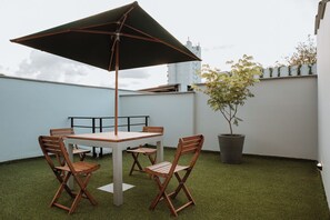 Una terraza en la azotea con una mesa, sillas, una sombrilla grande y una planta en maceta.