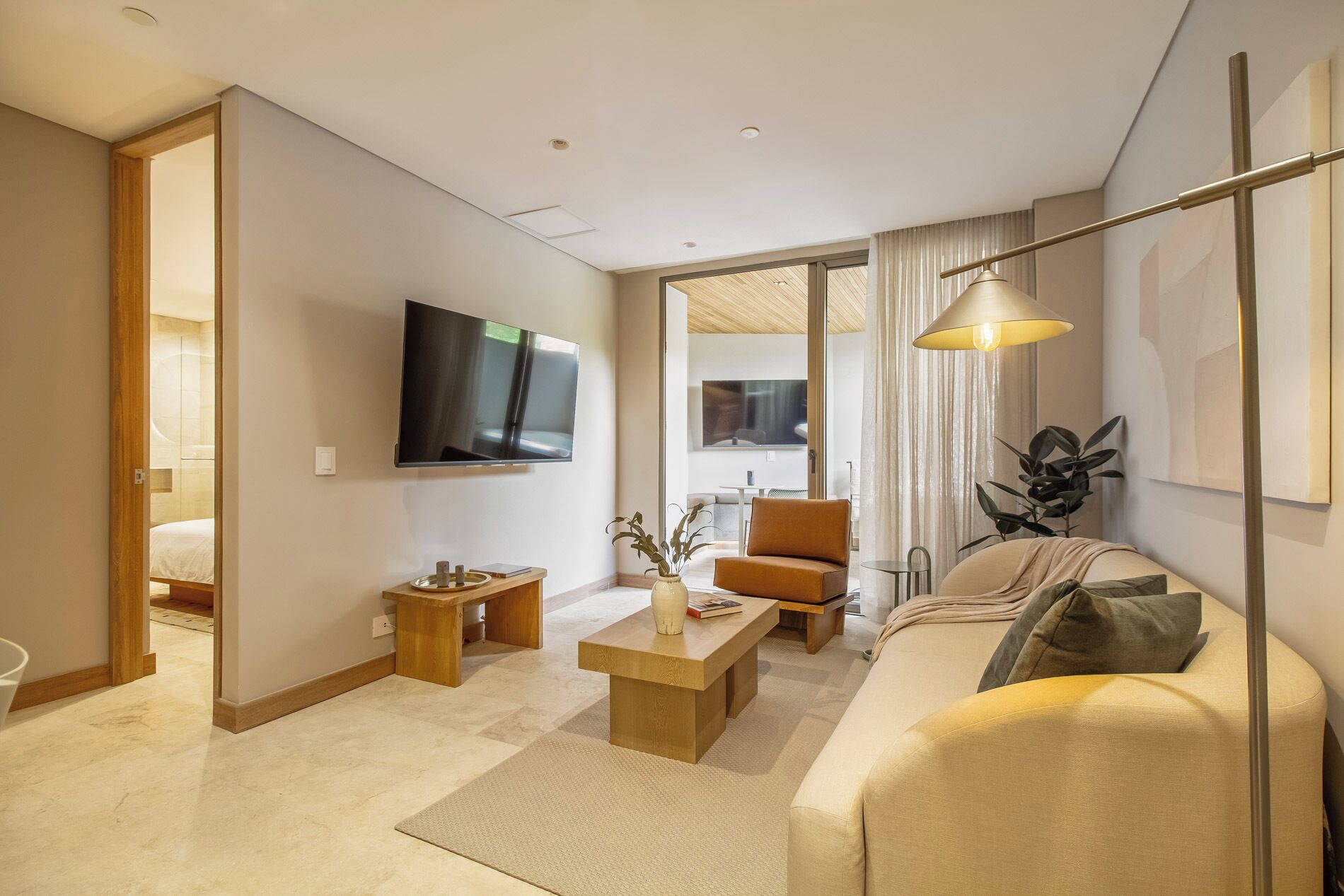 Una sala de estar moderna con televisor de pantalla plana, un sofá, una mesa de centro y un comedor visible a través de una puerta abierta.
