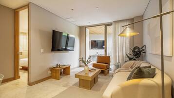 Una sala de estar moderna con televisor de pantalla plana, un sofá, una mesa de centro y un comedor visible a través de una puerta abierta.