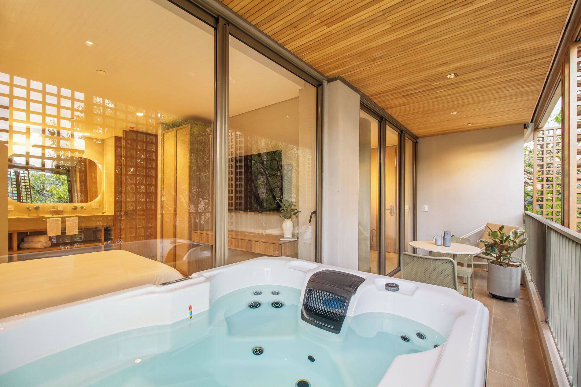 Un baño moderno con una bañera grande, cabina de ducha con mampara de vidrio y un balcón con mobiliario exterior.