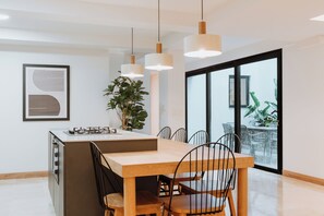 Una cocina moderna con una isla central, luces colgantes y un comedor con sillas.